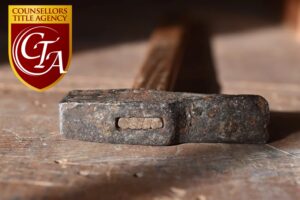 Close-up of an old, rusty hammer on a wooden surface with a blurred background.