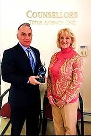 Man holding an award stands next to a smiling woman in a patterned blouse.
