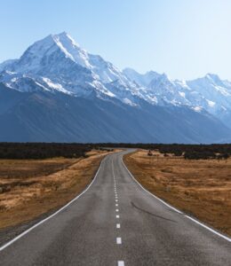 Open road leading to towering snow-capped mountains.