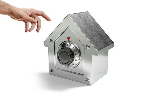 Metallic house-shaped combination lock with a hand nearby.