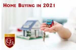 A hand holds a small house model and keys with a blurred house model in the background.