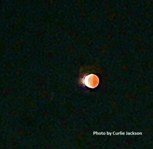 A reddish moon during a lunar eclipse against a dark sky.