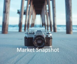 Vintage camera on sandy beach under pier with ocean background.