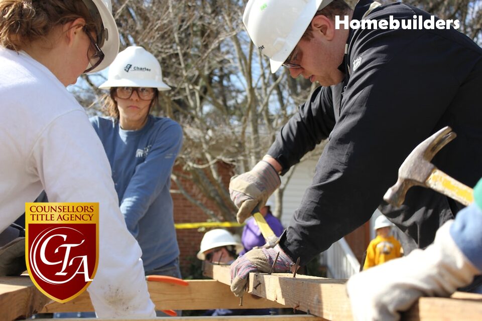 Volunteers wearing hard hats collaborate on a woodworking project outdoors.