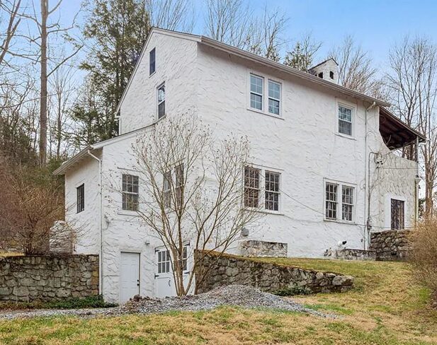 White two-story house with a stone foundation and leafless trees in front.