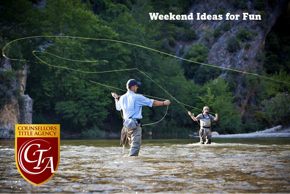 Two people fly fishing in a river surrounded by forest.