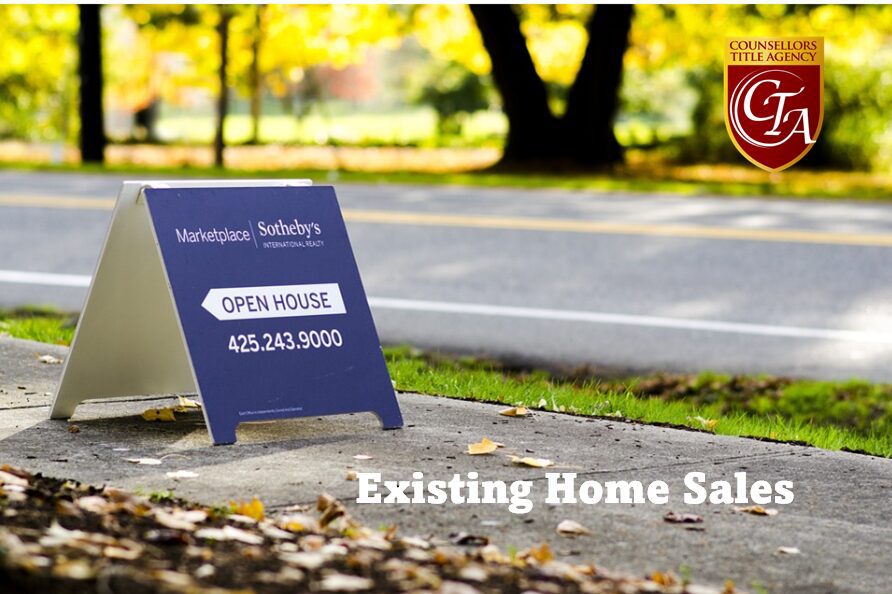 Real estate open house sign by a road surrounded by autumn leaves.
