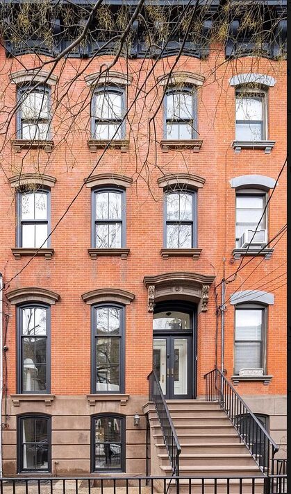 Classic brick townhouse with tall windows and ornate entrance in an urban setting.