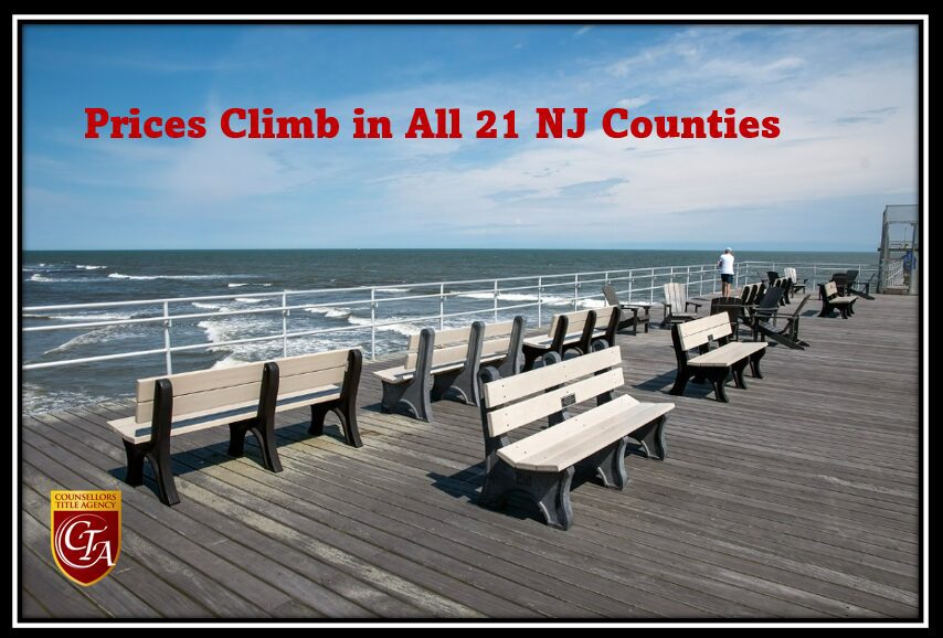 Empty benches on a wooden boardwalk overlooking the ocean under a blue sky.