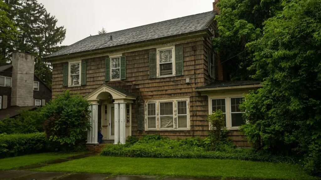 Classic two-story house with wooden shingles and lush greenery.