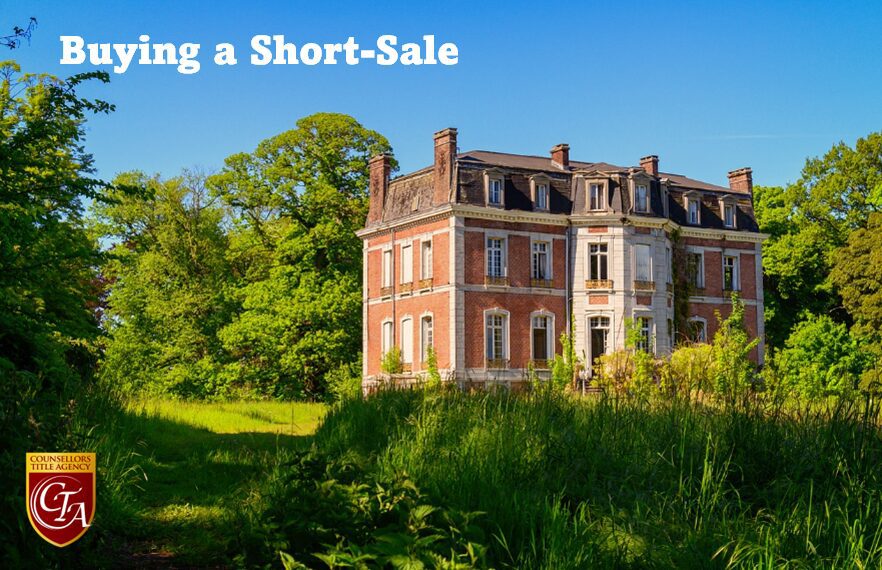 A large, old house surrounded by greenery under a clear blue sky.