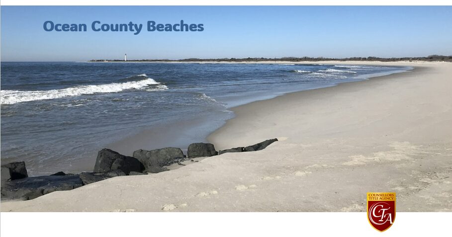 A sandy beach with gentle waves and rocks under a clear blue sky.