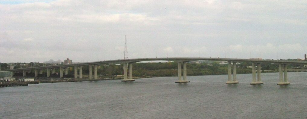A wide concrete bridge over a calm river with greenery in the background.