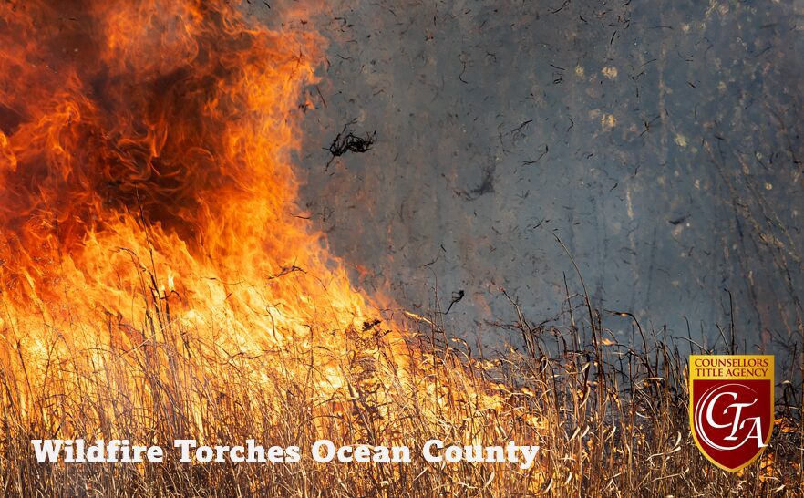 A wildfire rages on a hillside with a helicopter flying overhead.