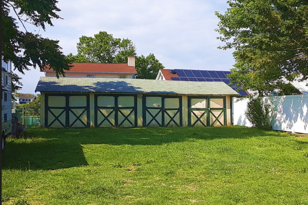 A sunny backyard with a green lawn and outbuildings under a blue sky.
