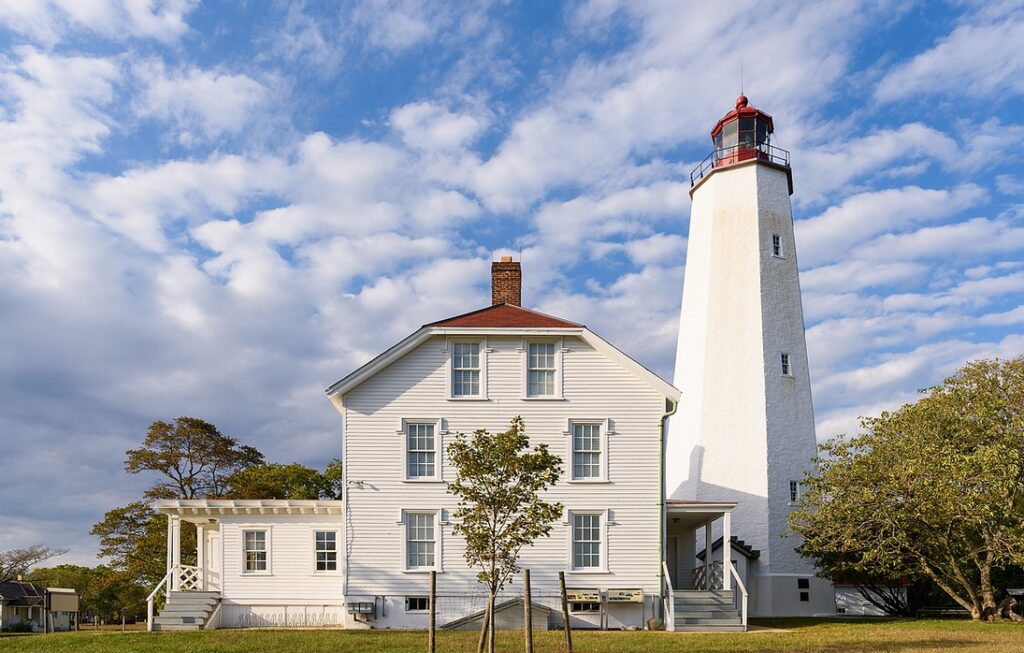 White lighthouse beside house, under blue sky.