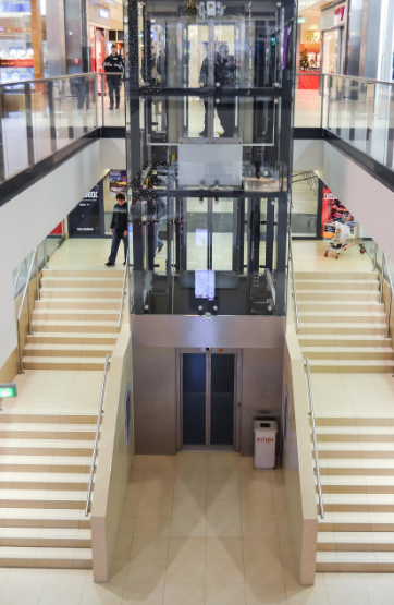 Modern indoor space with glass elevator and symmetrical staircases.